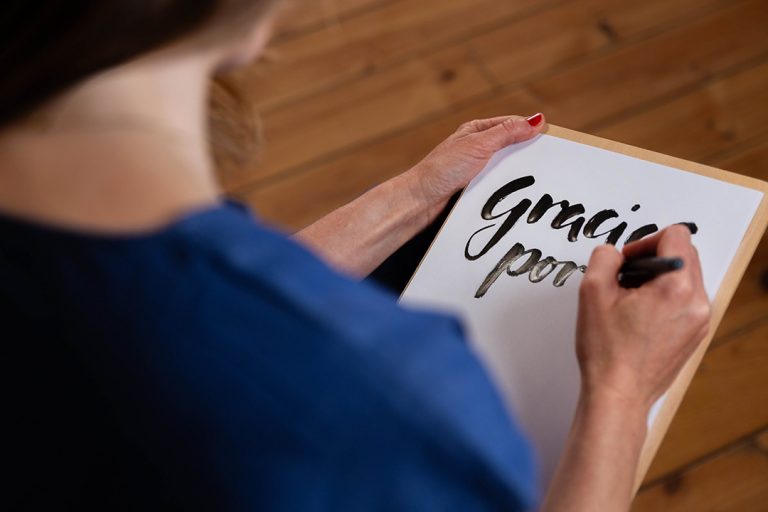 Grafikdesignerin zeichnet und setzt das Wort Gracias por ... schwarz/weiss mit Handlettering auffällig und schön in Szene