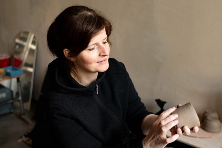 Portrait einer Keramikerin während sie ihr neues Werk, eine Tasse, betrachtet