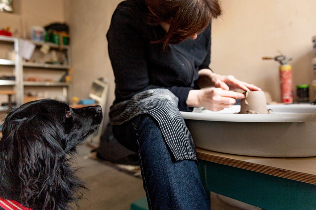 Die Keramikerin dreht an in einer Drehscheibe eine Tasse während ihr süßer Hund ihr dabei zuschaut