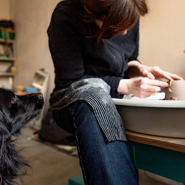 Die Keramikerin dreht an in einer Drehscheibe eine Tasse während ihr süßer Hund ihr dabei zuschaut