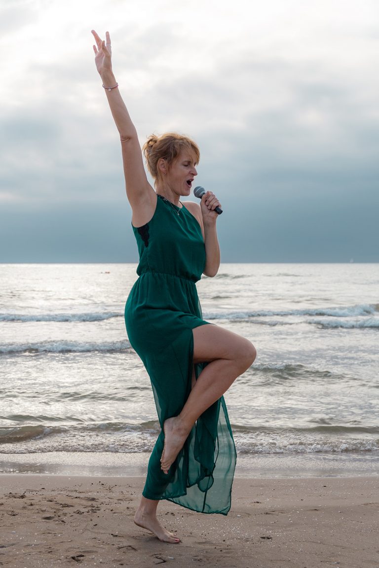 Sängerin performt, tanzt und singt mit voller Leidenschaft am Meer zum Sonnenuntergang