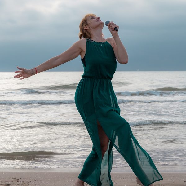 Sängerin singt und tanzt am Meer als wäre sie auf einer Bühne