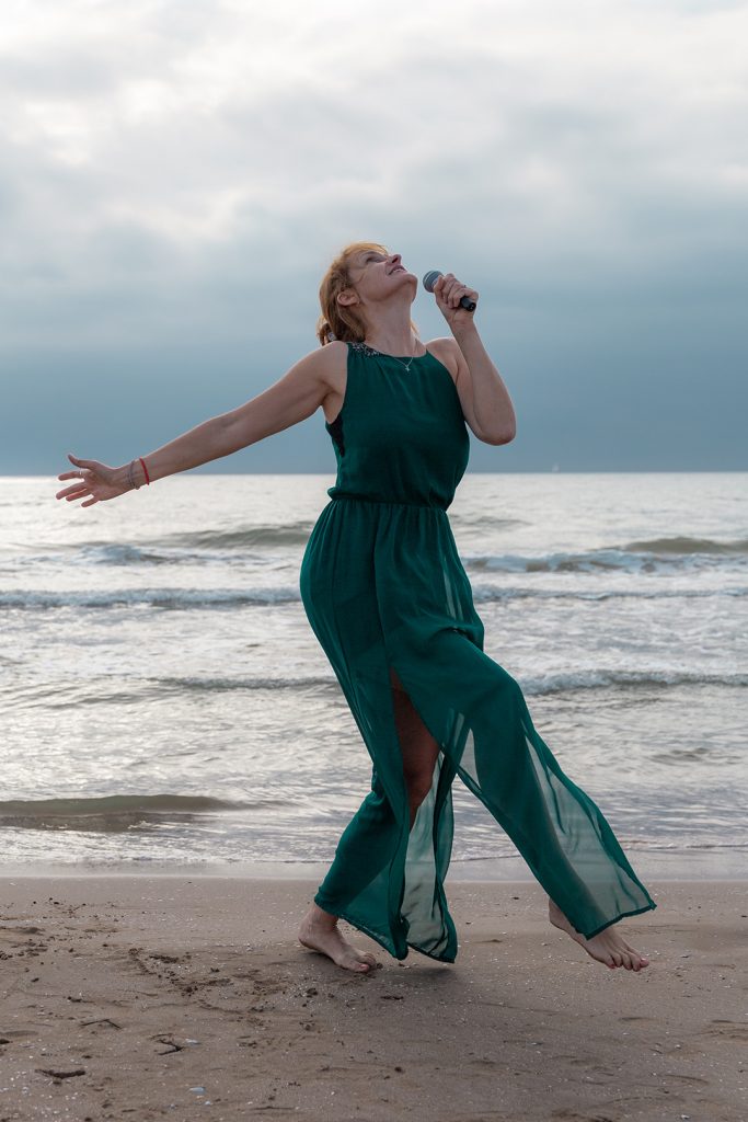 Sängerin singt und tanzt am Meer als wäre sie auf einer Bühne