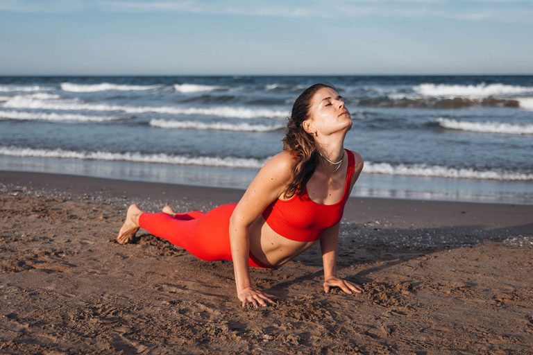 Yogalehrerin bei ihrer Yogapraxis am Strand mit Meer im Hintergrund