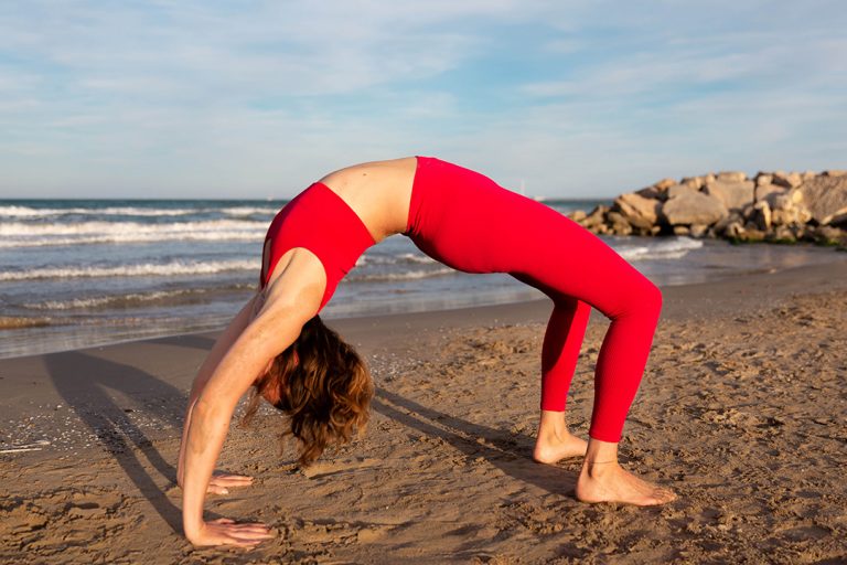 Yogalehrerin bei ihrer Yogapraxis am Strand mit Meer im Hintergrund